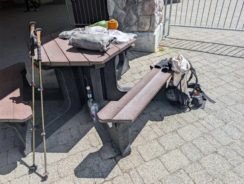Sac à dos, bâtons de marche et nourriture posés sur une table de pique-nique