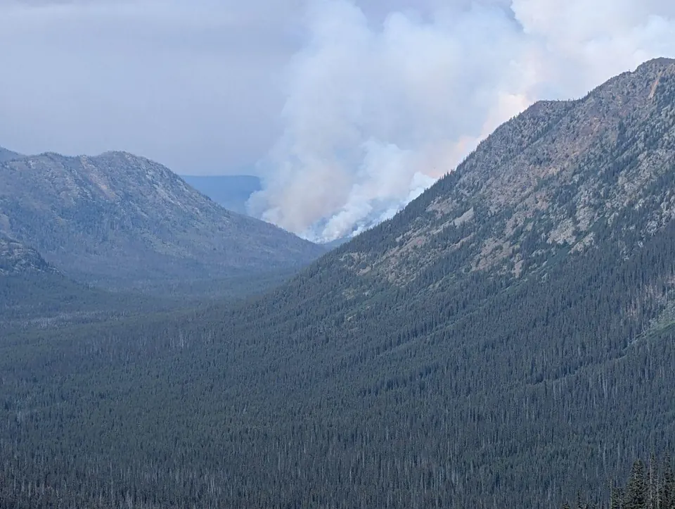 Panache de fumée s'élevant entre deux montagnes boisées