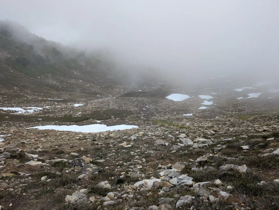 Versant rocheux parsemé de plaques de neige dans un épais brouillard