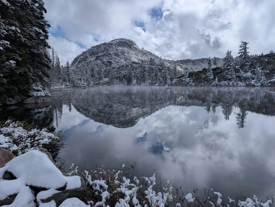 Lac de montagne reflétant une falaise et des arbres enneigés