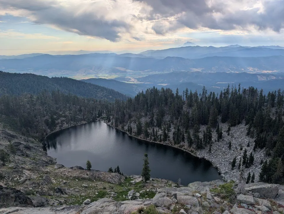 Lac sombre dans un cirque boisé face à des montagnes lointaines