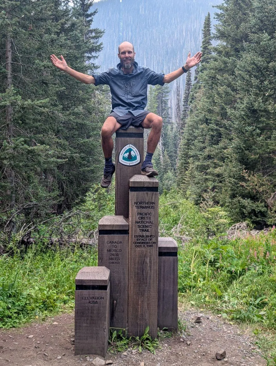 Randonneur assis les bras levés sur un monument du Pacific Crest Trail