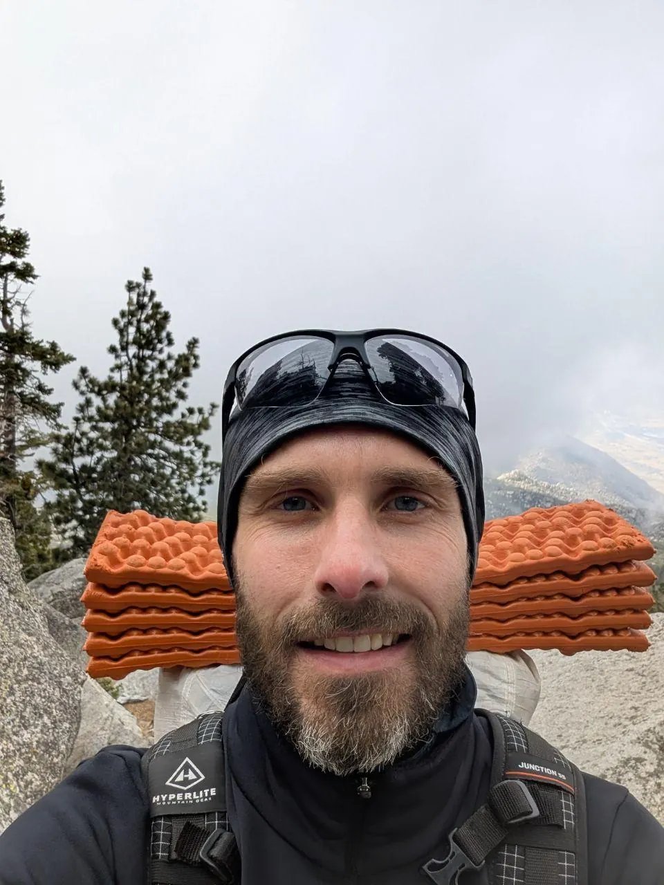 Autoportrait d'un randonneur barbu avec un matelas orange fixé au sac