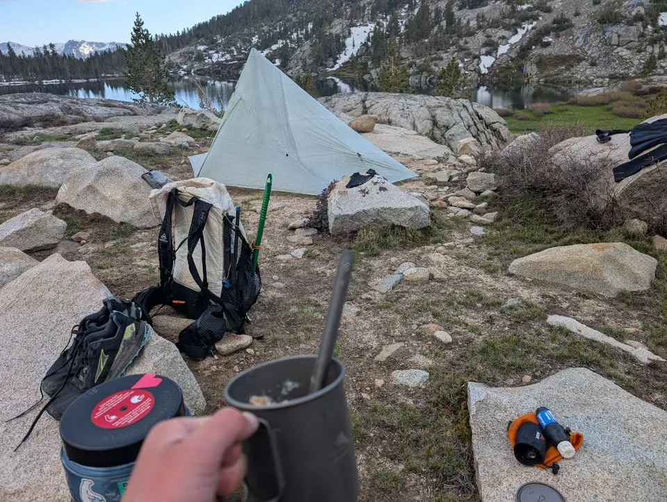 Tente et sac à dos sur un campement rocheux avec une tasse au premier plan