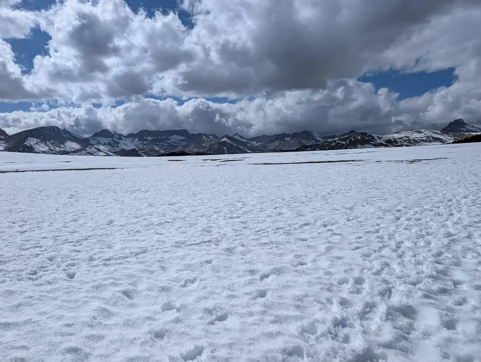 Grande étendue de neige bordée de crêtes rocheuses sous des nuages imposants