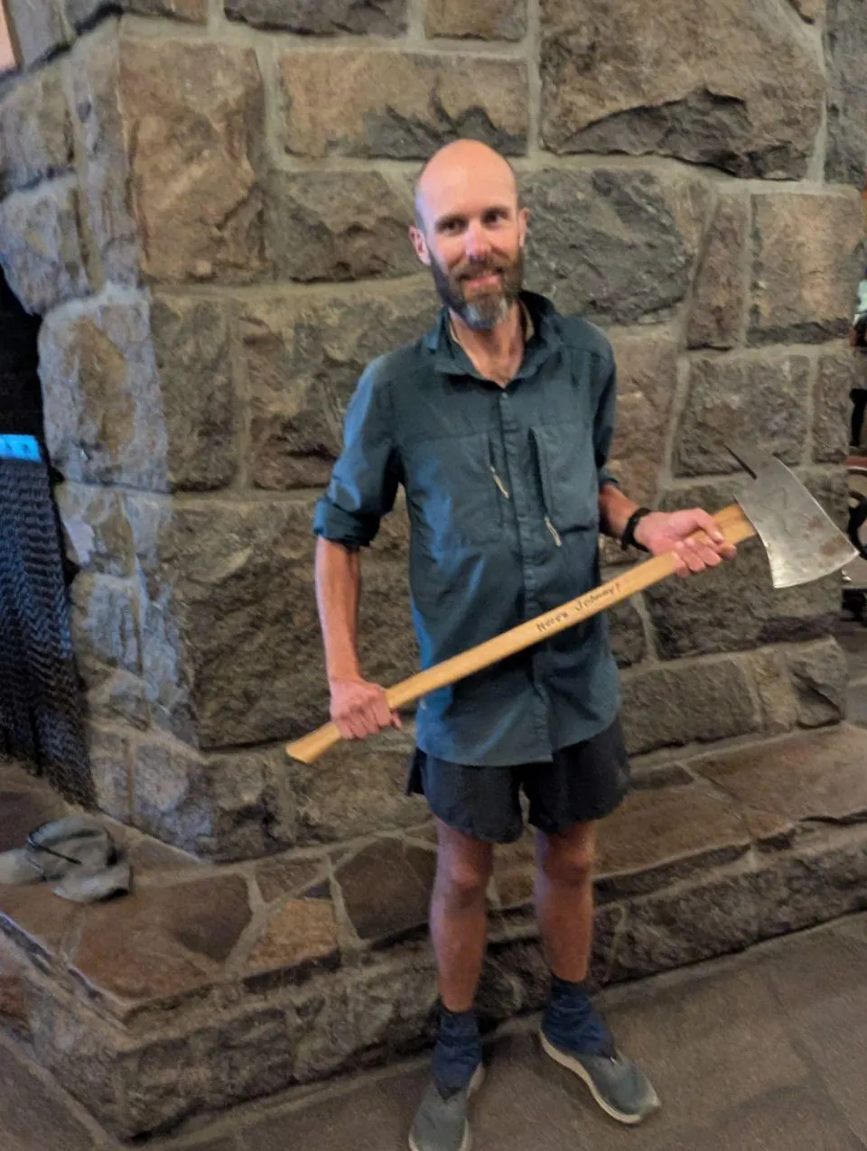 Randonneur tenant un manche en bois devant une grande cheminée en pierre
