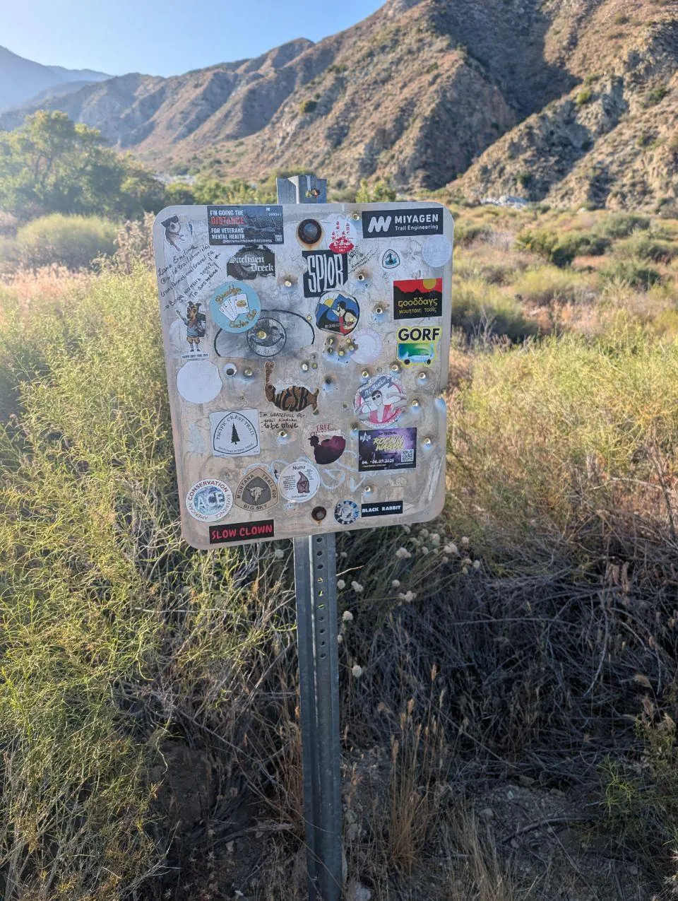 Panneau de sentier couvert d'autocollants dans une vallée aride
