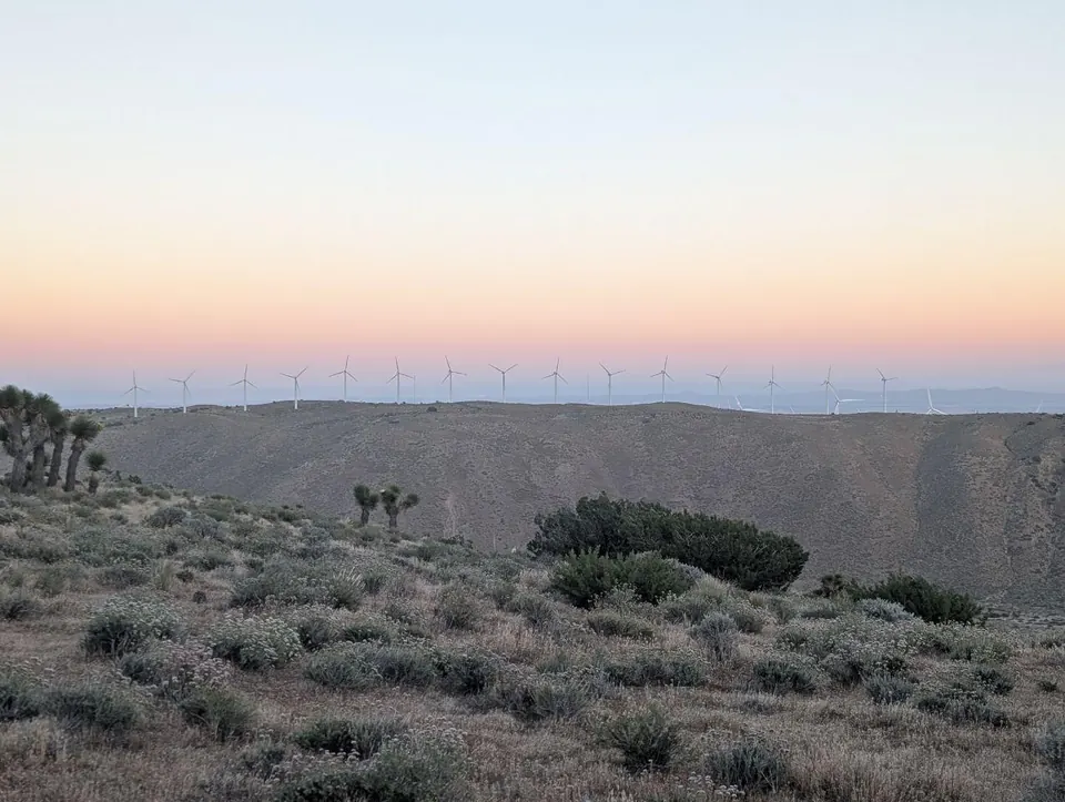 Éoliennes alignées à l'horizon dans un paysage désertique au crépuscule
