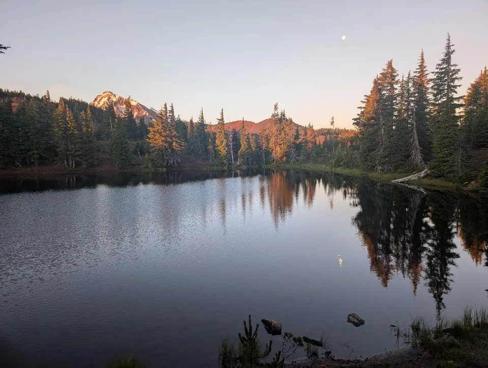 Lac de montagne reflétant des sapins et des sommets au coucher du soleil