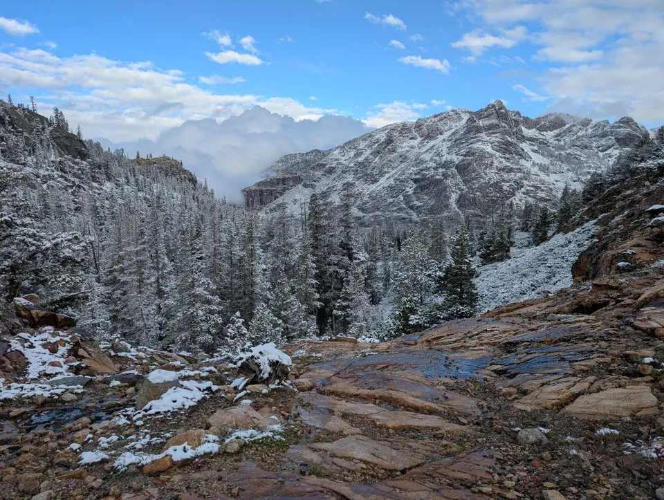 Vallon montagneux enneigé sous un ciel bleu et nuageux