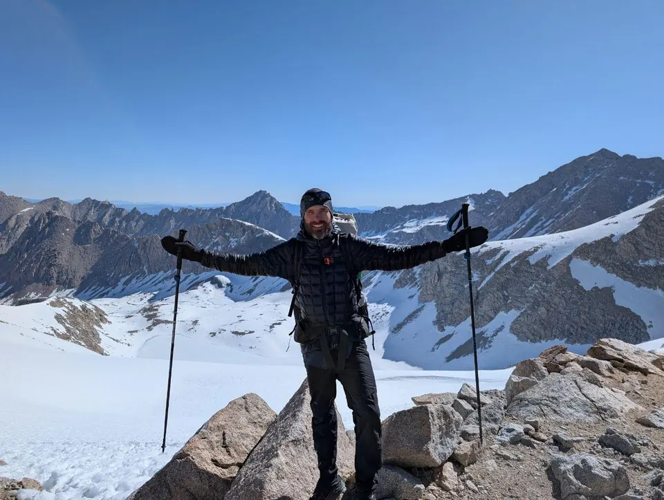 Randonneur debout sur un sommet rocheux devant des montagnes enneigées