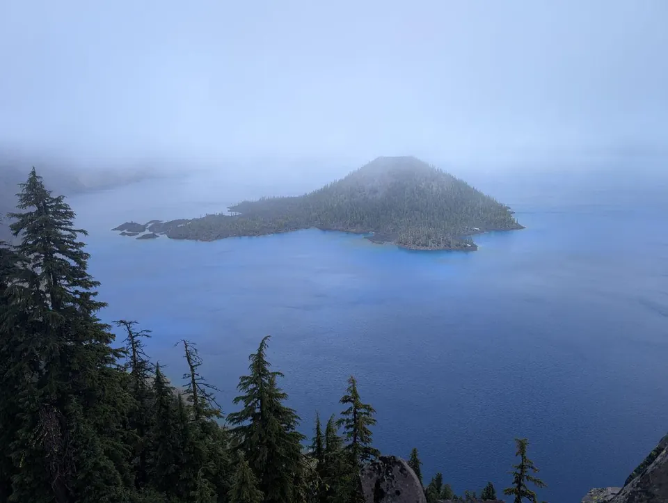 Île boisée émergeant d'un lac enveloppé de brume