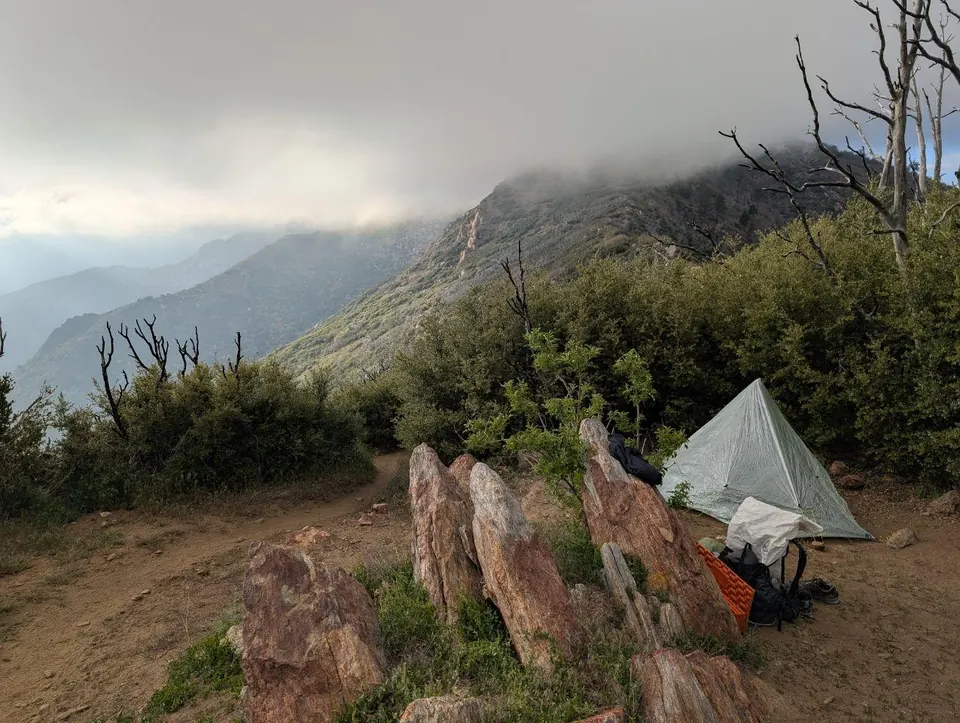 Tente légère dressée derrière des rochers sous un ciel d'orage