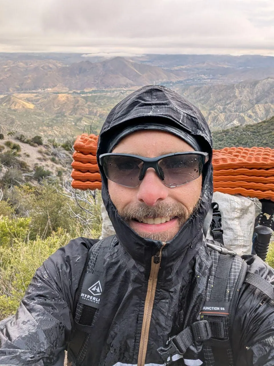 Randonneur souriant sous une capuche avec son sac chargé