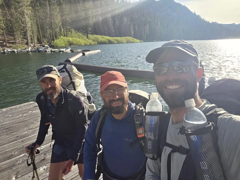 Trois randonneurs souriants sur un ponton au bord d'un lac