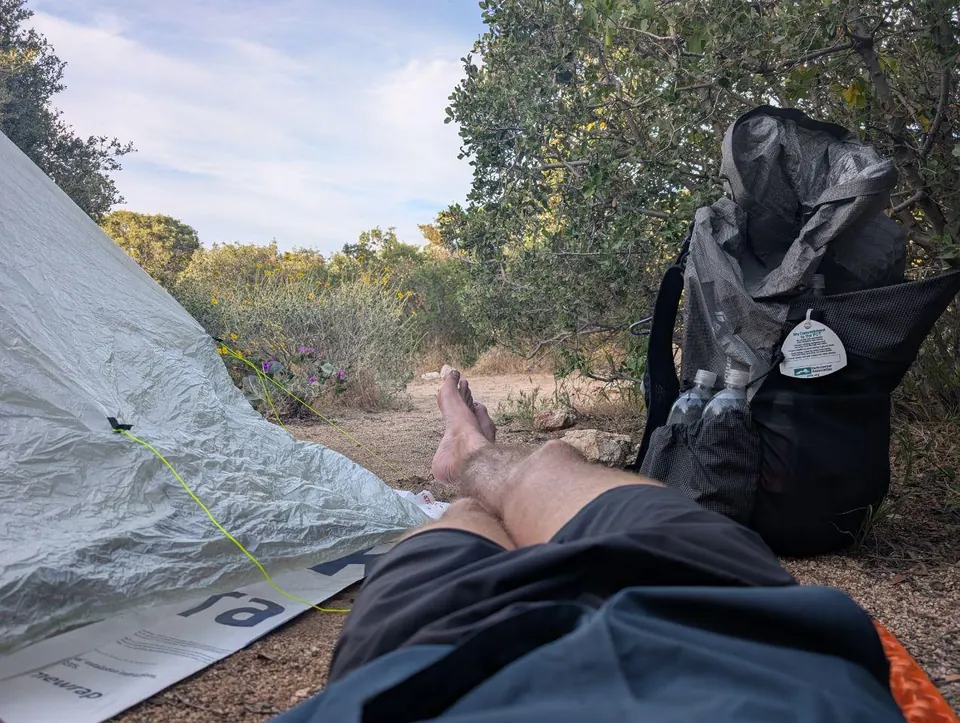 Jambes allongées devant une tente avec un sac à dos