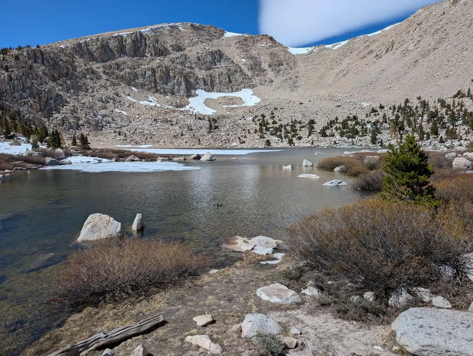 Petit lac alpin bordé de rochers et de plaques de neige